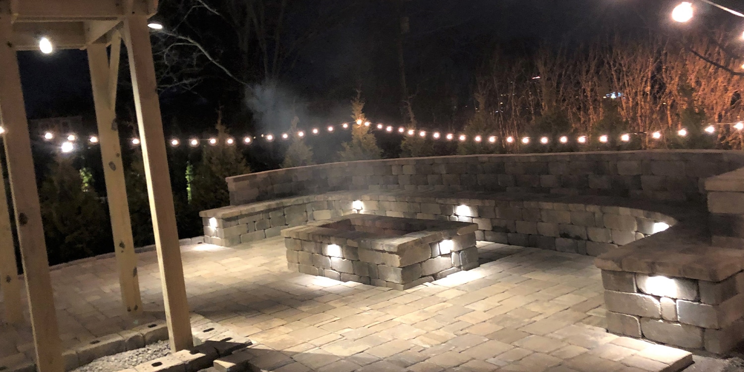 A lit up outdoor living space with Garden lighting offered by Opportunity Landscapes and Nursery
